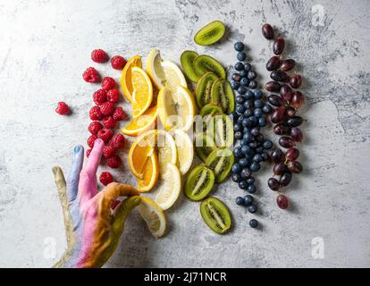 Fruits coupés et disposés dans l'ordre des couleurs arc-en-ciel. Un peint à la main dans des couleurs arc-en-ciel prend un fruit. Gay Pride Day, concept LGBT. Banque D'Images