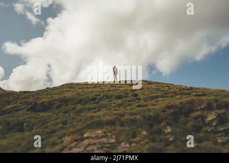 Vue éloignée d'un couple de mariage debout dans un champ sur une colline. Le sommet de la montagne. Prise de photos. Banque D'Images