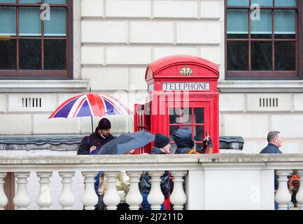 Des piétons marchent devant une personne tenant un parapluie drapeau de l'Union à côté d'une boîte téléphonique rouge traditionnelle à Westminster, dans le centre de Londres. Banque D'Images