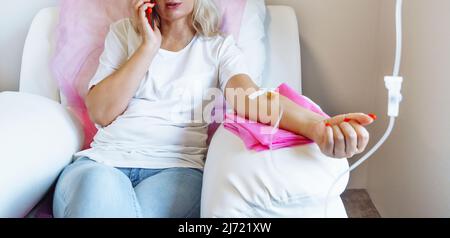 Femme à l'hôpital parlant au téléphone mobile pendant que l'aiguille est dans le bras, vitamine Therapy IV perfusion goutte dans le sang des femmes Banque D'Images