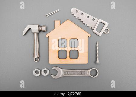 Outils à main et fixations indispensables disposés autour d'un modèle de maison plate miniature sur fond gris Banque D'Images