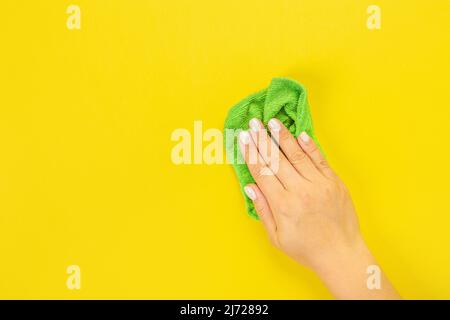 La main d'une femme au foyer tient un chiffon pour épousseter ou laver. Espace vide pour le texte ou le logo sur fond jaune. Début du printemps ou nettoyage régulier. Nettoyage Banque D'Images