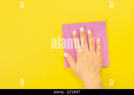 La main d'une femme au foyer tient un chiffon pour épousseter ou laver. Espace vide pour le texte ou le logo sur fond jaune. Début du printemps ou nettoyage régulier. Nettoyage Banque D'Images