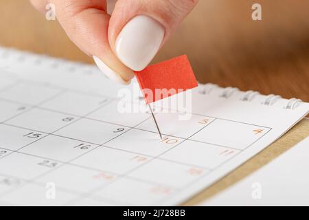 Les mains corrigeant l'horaire des notes, la vignette du drapeau rouge dans le calendrier pour la réunion et le rappel de rendez-vous Banque D'Images