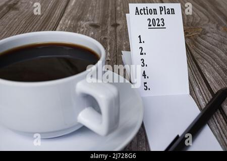 Livre avec plan d'action 2023 texte et café sur bureau en bois. Résolutions et plan de la nouvelle année. Banque D'Images