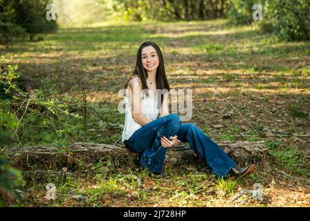 Une belle jeune fille de brunette adolescente heureuse assise à l'extérieur sur un log Hapy et souriant avec l'espace de copie Banque D'Images