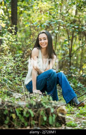 Une belle jeune fille de brunette adolescente heureuse assise à l'extérieur sur un log Hapy et souriant avec l'espace de copie Banque D'Images