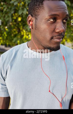 Portrait à la taille d'un beau sportif afro-américain debout à l'extérieur, en écoutant de la musique à l'aide d'écouteurs et en regardant loin Banque D'Images
