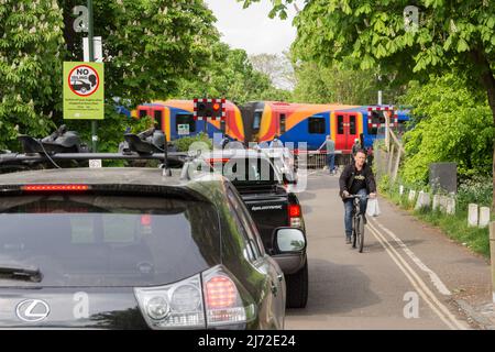 Des voitures stationnaires faisant la queue et tournant au ralenti tandis qu'un train South Western Railway passe la boîte de signalisation de la route Vine de Network Rail à Barnes, Londres, SW13, Angleterre, Royaume-Uni