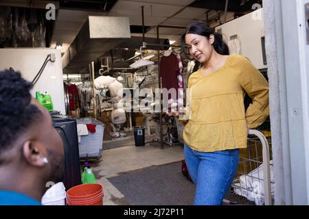 Homme et femme travaillant à des nettoyeurs à sec prenant une pause et parlant. Banque D'Images