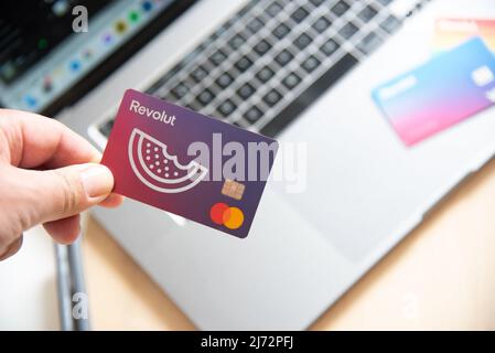 Main humaine tenant une carte de débit Revolut. Paiement numérique de l'application de téléphone mobile en ligne avec un ordinateur portable Banque D'Images