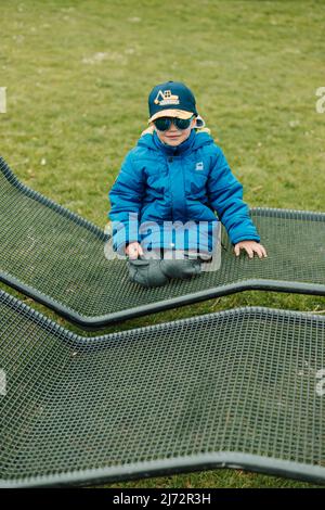 Un petit garçon en lunettes de soleil rampent sur un banc de parc Banque D'Images