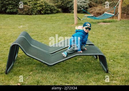 Un petit garçon en lunettes de soleil rampent sur un banc de parc Banque D'Images