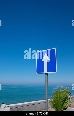 Panneau carré avec flèche blanche sur fond bleu ciel. Il indique une route à sens unique Banque D'Images