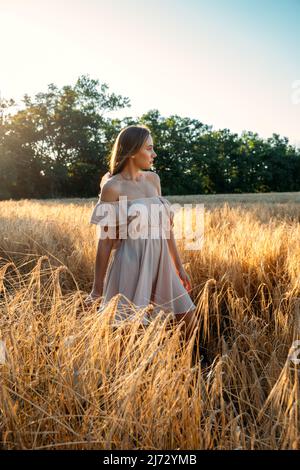 Connectez-vous à la nature, ralentissez, soyez présent, entrez dans vos sens. Paisible seule jeune femme en robe marchant sur le champ de blé au coucher du soleil le jour d'été Banque D'Images