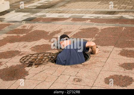 Un travailleur sort d'un trou d'homme ouvert dans la route. Trou d'homme dangereux ouvert non protégé sur la route. Accident avec un trou d'égout dans la ville. Le con Banque D'Images