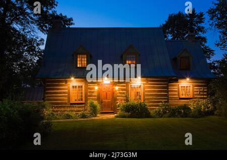 Vieux 1800s maison en rondins de style Canadiana à deux étages avec cour avant paysagée et pelouse en herbe au crépuscule. Banque D'Images