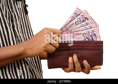 Main de femme équitable porte-monnaie marron avec des notes ghanéennes cedi, main retirant l'argent de la bourse isolée sur blanc. Retirer l'argent de la poche Banque D'Images