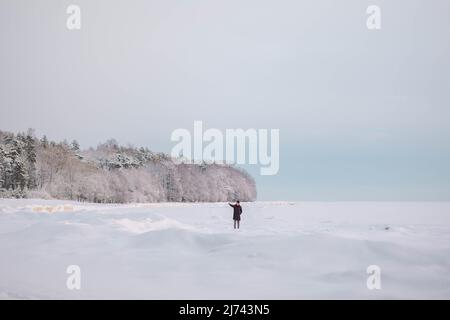 Magnifique paysage d'hiver dans un style minimaliste. Petites figures de personnes sur le champ de neige blanche et de forêt à l'horizon. Ambiance claire et aérée et palette de couleurs claires. Banque D'Images