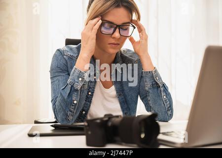 Femme photographe souffrant d'un mal de tête sur son lieu de travail à la maison Banque D'Images