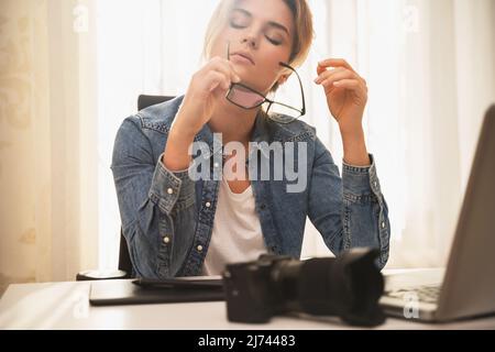 Femme photographe souffrant d'un mal de tête sur son lieu de travail à la maison Banque D'Images