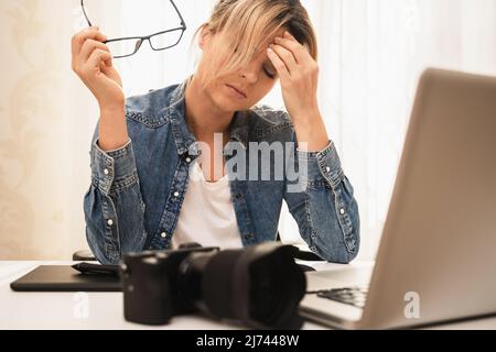 Femme photographe souffrant d'un mal de tête sur son lieu de travail à la maison Banque D'Images