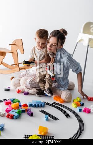 petit garçon avec une jeune mère jouant avec le chemin de fer jouet sur blanc Banque D'Images