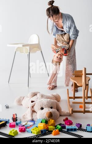 femme excitée jouant avec son fils près de cheval de bascule et chien jouet sur blanc Banque D'Images