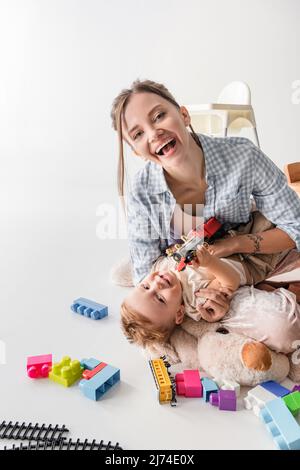 femme en train de rire regardant l'appareil photo tout en jouant avec son fils sur blanc Banque D'Images