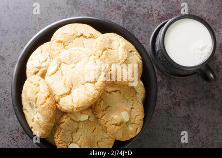 Petits gâteaux cuits au caramel au chocolat blanc et aux noix de macadamia servis avec une tasse de lait sur la table en gros plan. Vue horizontale du dessus Banque D'Images