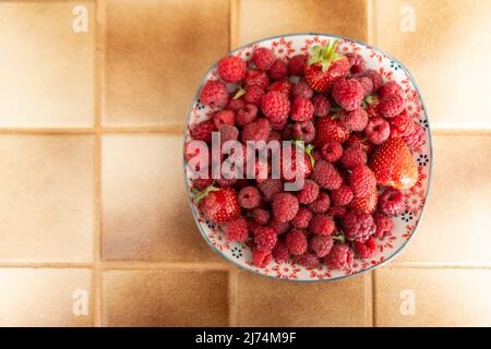 Dessus et grande vue d'une assiette de fraises fraîches et framboises dans une cuisine, posée sur un carrelage beige Banque D'Images