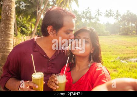 une famille indienne heureuse tenant un verre de jus de canne frais avec un tube en métal écologique et prenant un portrait selfie sur un smartphone. voyagez et faites des économies Banque D'Images