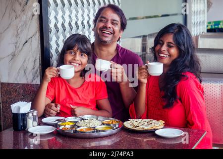 belle mère et père heureux manger thali avec fille dans le café et boire masala chai Banque D'Images