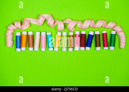 Ensemble de fils multicolores pour la couture et ruban de mesure avec un espace pour le texte sur fond vert, vue de dessus. Adaptation et travail des aiguilles Banque D'Images