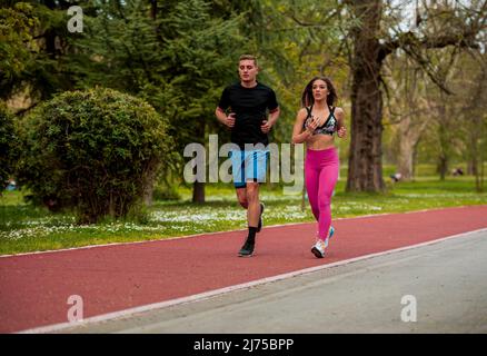 Jeune couple de sportifs en forme, garçon et fille courant tout en faisant de l'exercice sur les pistes rouges à l'extérieur Banque D'Images