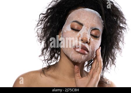 Belle femme noire avec une peau lisse appliquant masque de feuille de visage Banque D'Images