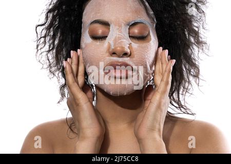 Belle femme noire avec une peau lisse appliquant masque de feuille de visage Banque D'Images