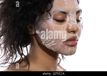 Belle femme noire avec une peau lisse appliquant masque de feuille de visage Banque D'Images