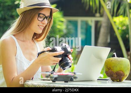 Une photographe féminine insère ou retire une carte mémoire dans son appareil photo reflex numérique professionnel alors qu'elle est assise sur un bureau avec son ordinateur portable au paradis Beach Green Banque D'Images