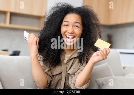 Une adolescente multiraciale surjoyeuse rêvant d'acheter à l'avenir, dépensant de l'argent du premier salaire, tenant une carte de crédit et un téléphone mobile Banque D'Images