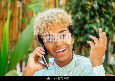 émerveillement blond attrayant cheveux maurly africaine fille américaine commérages avec un ami par téléphone au café tropical Banque D'Images