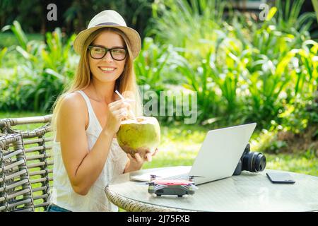 Jeune photographe femme se sentant heureuse becouse elle obtient de l'argent en ligne tout en s'asseyant au café tropical Banque D'Images