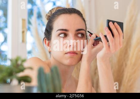 Femme en beauté sesion cheveux en enlevant ses sourcils d'oeil devant un miroir avec des plantes autour à la maison Banque D'Images