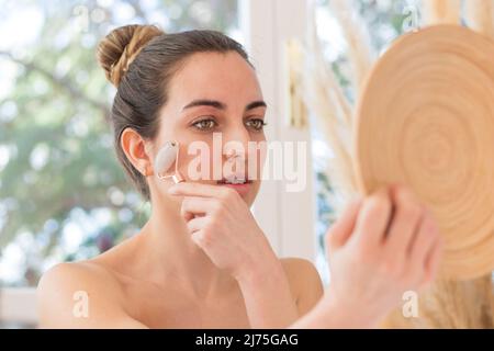 Portrait d'une jeune femme de style nautique utilisant un rouleau de quartz rose sur son visage comme concept de bien-être, de beauté et de soins de la peau Banque D'Images