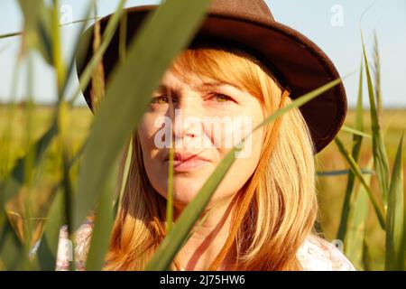 Flou artistique gros plan portrait extérieur de la belle jeune femme blonde près du roseau et de l'herbe de pampas. Ombres d'art végétal. Cow-girl sur la prairie. Santé mentale Banque D'Images