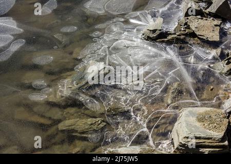 Texture et détail de fragments brisés de glace piégés entre les pierres d'un lac gelé dans une montagne himalayenne éloignée. Banque D'Images