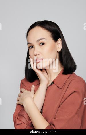 Portrait d'une jeune femme asiatique sérieuse avec maquillage naturel touchant son propre visage sur fond blanc Banque D'Images