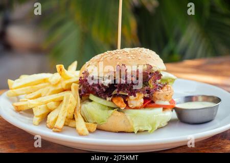 hamburger aux crevettes et alevins français sur la mer tropicale de table, palmiers et fond de plage Banque D'Images