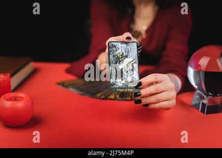 KIEV, UKRAINE - 23 FÉVRIER 2022 : vue rognée d'une couche de suies brouillées montrant une carte de tarot près de l'orbe et des bougies Banque D'Images