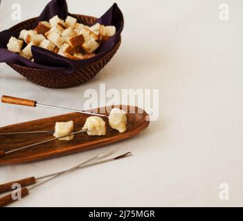 Trois morceaux de pain trempés à la fondue au fromage sur la fourche; bol de cubes de pain en arrière-plan Banque D'Images